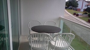 Een balkon met een ronde tafel en vier witte stoelen.