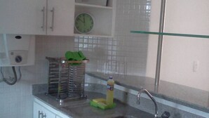Een keuken met witte kastjes, een roestvrijstalen spoelbak, een groene afwasschotel, een fles afwasmiddel en een klok aan de muur.