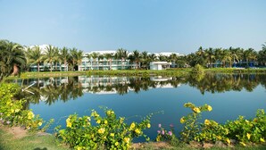 Un hotel con un estanque reflectante, palmeras y un cielo azul despejado.