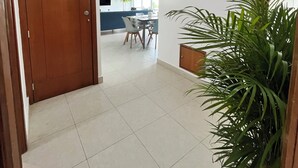 Un pasillo con una puerta de madera, un comedor con mesa y sillas, y una planta en maceta.