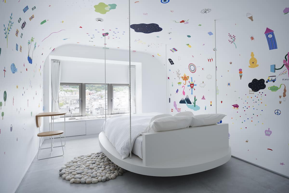 A modern bedroom with a circular bed, a view of the city, and playful wall decals.