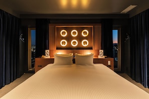 A modern hotel room with a large bed, a wall-mounted light panel, and a city view.