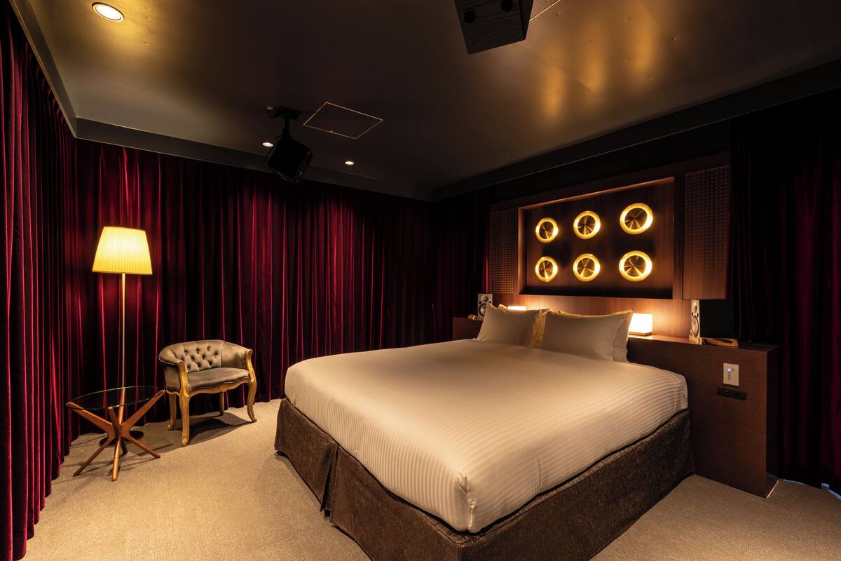 A spacious bedroom with a large bed, a seating area with a chair, and a wall-mounted light fixture.