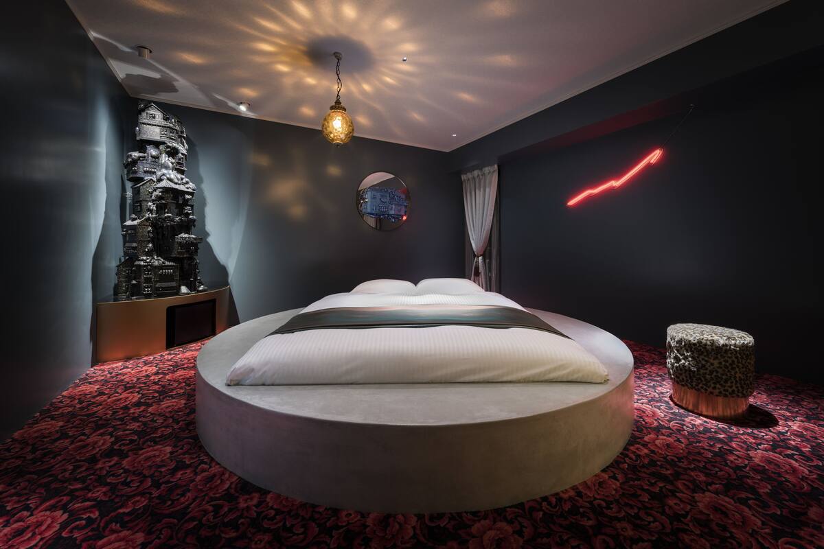A modern bedroom with a circular bed, a decorative wall sculpture, a round mirror, and a neon light.