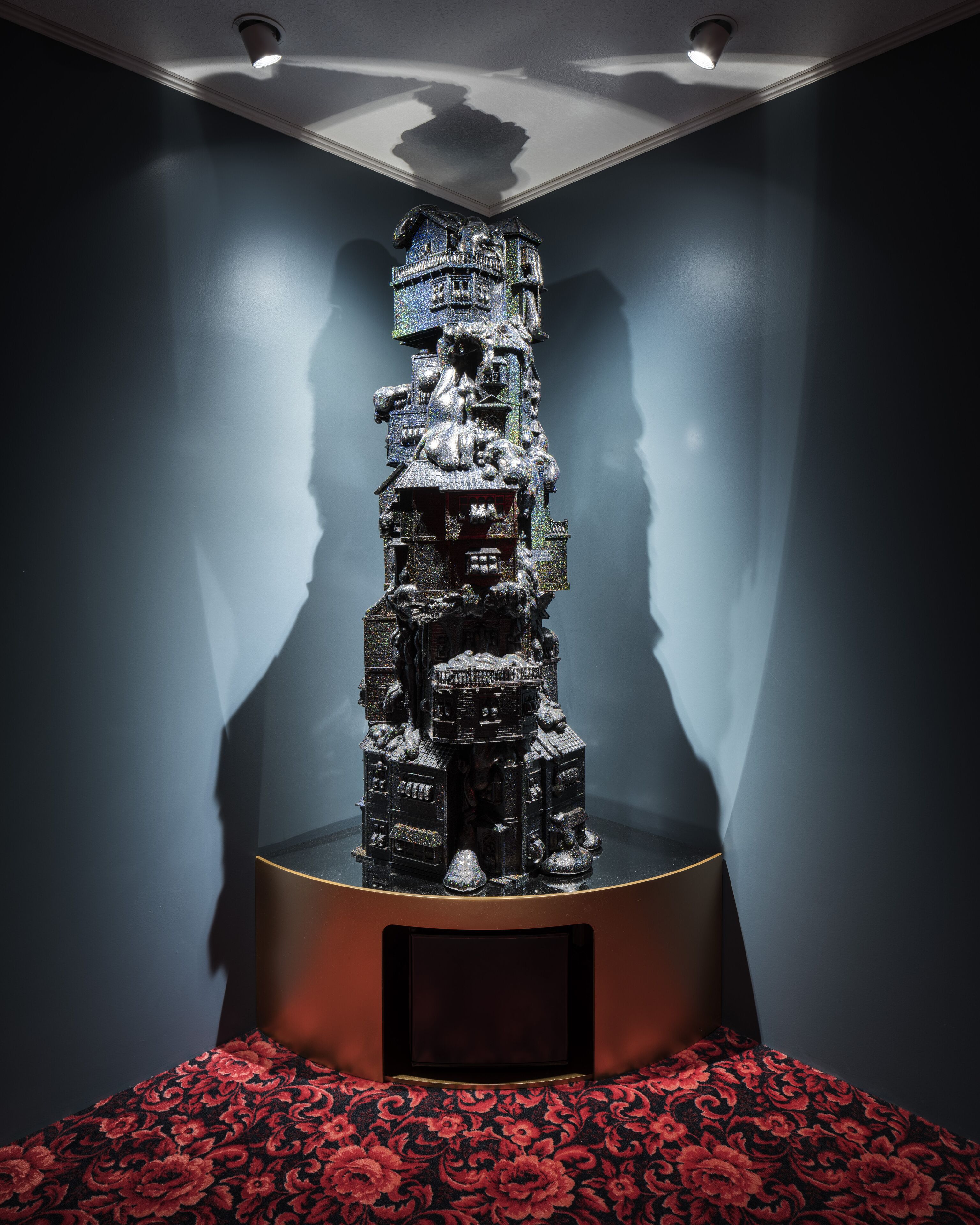 A sculpture with a dark base and a reflective surface, surrounded by a patterned carpet.