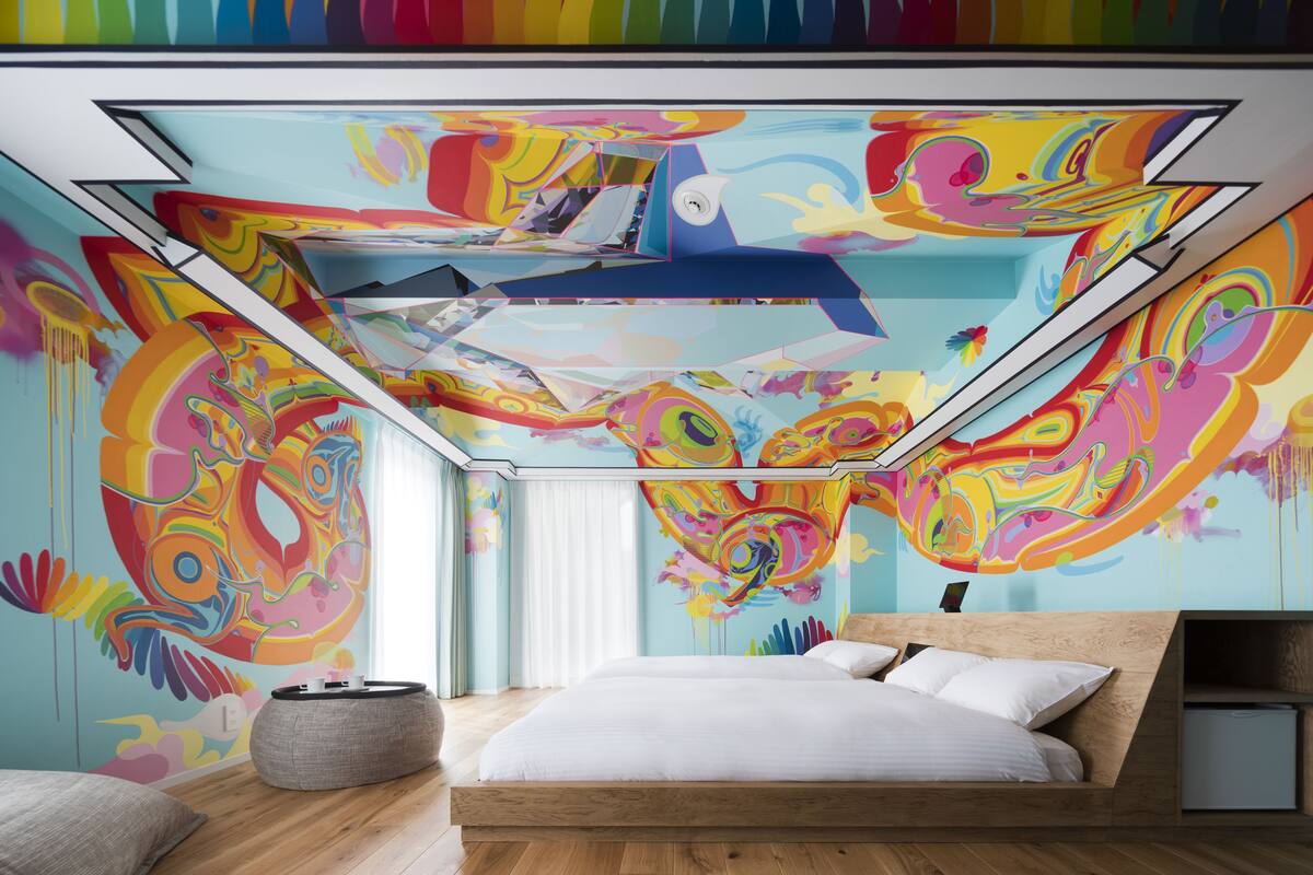 A modern bedroom with a colorful abstract mural, a large bed, and a skylight.