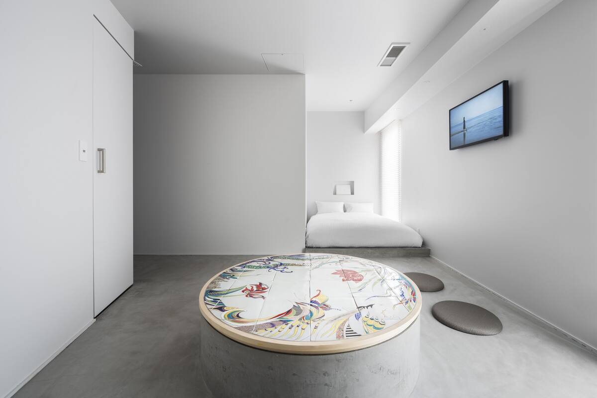 A modern hotel room with a round floor rug, a bed, a television, and a minimalist design.