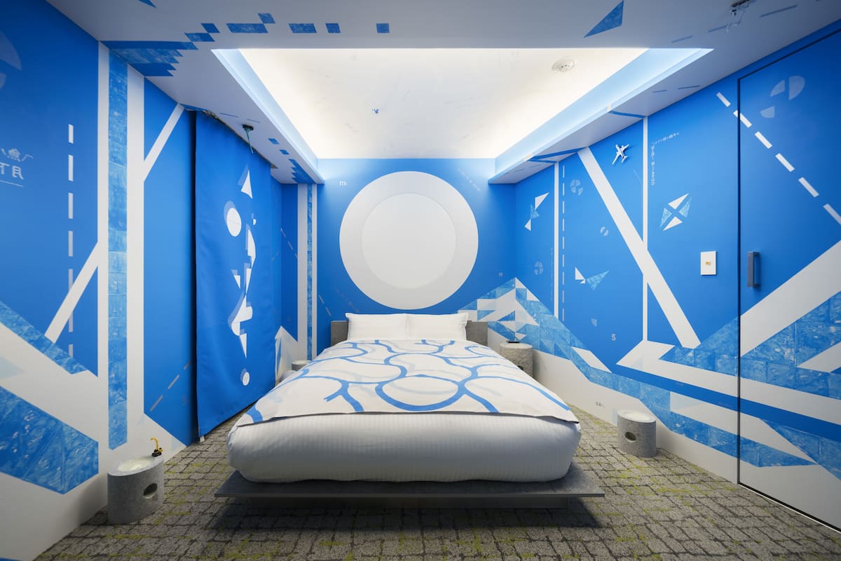 A modern bedroom with a skylight, a bed with a geometric-patterned bedspread, and walls decorated with abstract designs and shapes.
