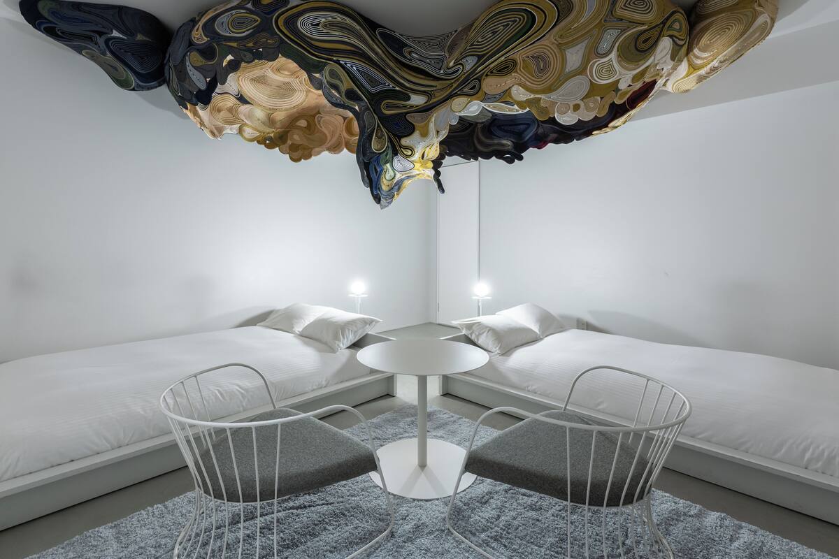 A modern room with a unique ceiling design, a round table, and two white beds.