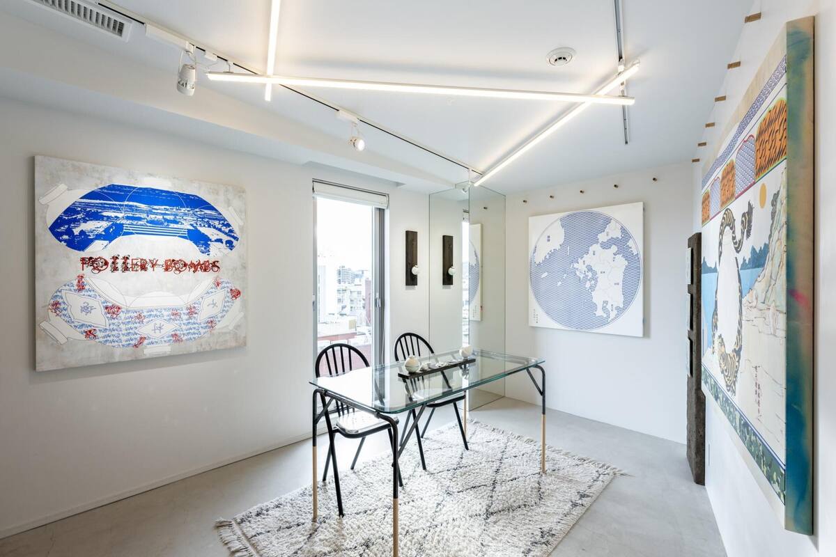 A modern art gallery with a glass table and chairs, surrounded by large artworks on the walls.