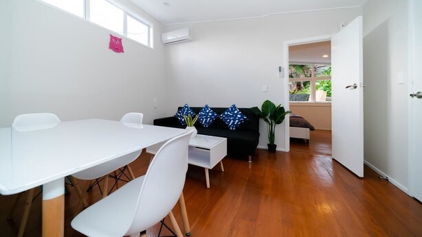 A modern living room with a white table and chairs, a black sofa with patterned cushions, and a wooden floor. - Takapuna Central Spacious & New Home (Auckland)