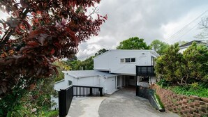 A modern two-story house with a covered driveway and a brick wall on one side. - Takapuna Central Spacious & New Home (Auckland)