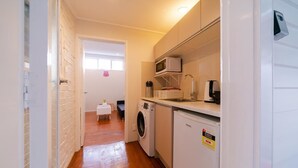 A compact kitchen with a washing machine, microwave, and a small refrigerator. - Takapuna Central Spacious & New Home (Auckland)