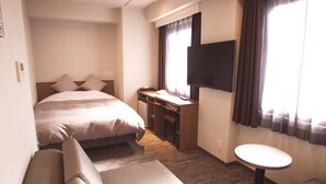 Una habitación de hotel con cama, escritorio, televisor, sofá y una pequeña mesa.
