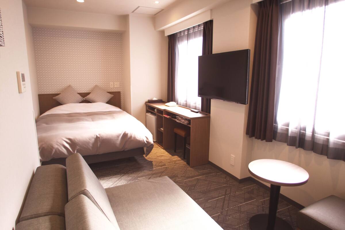 A hotel room with a bed, a desk, a TV, a sofa, and a small table.