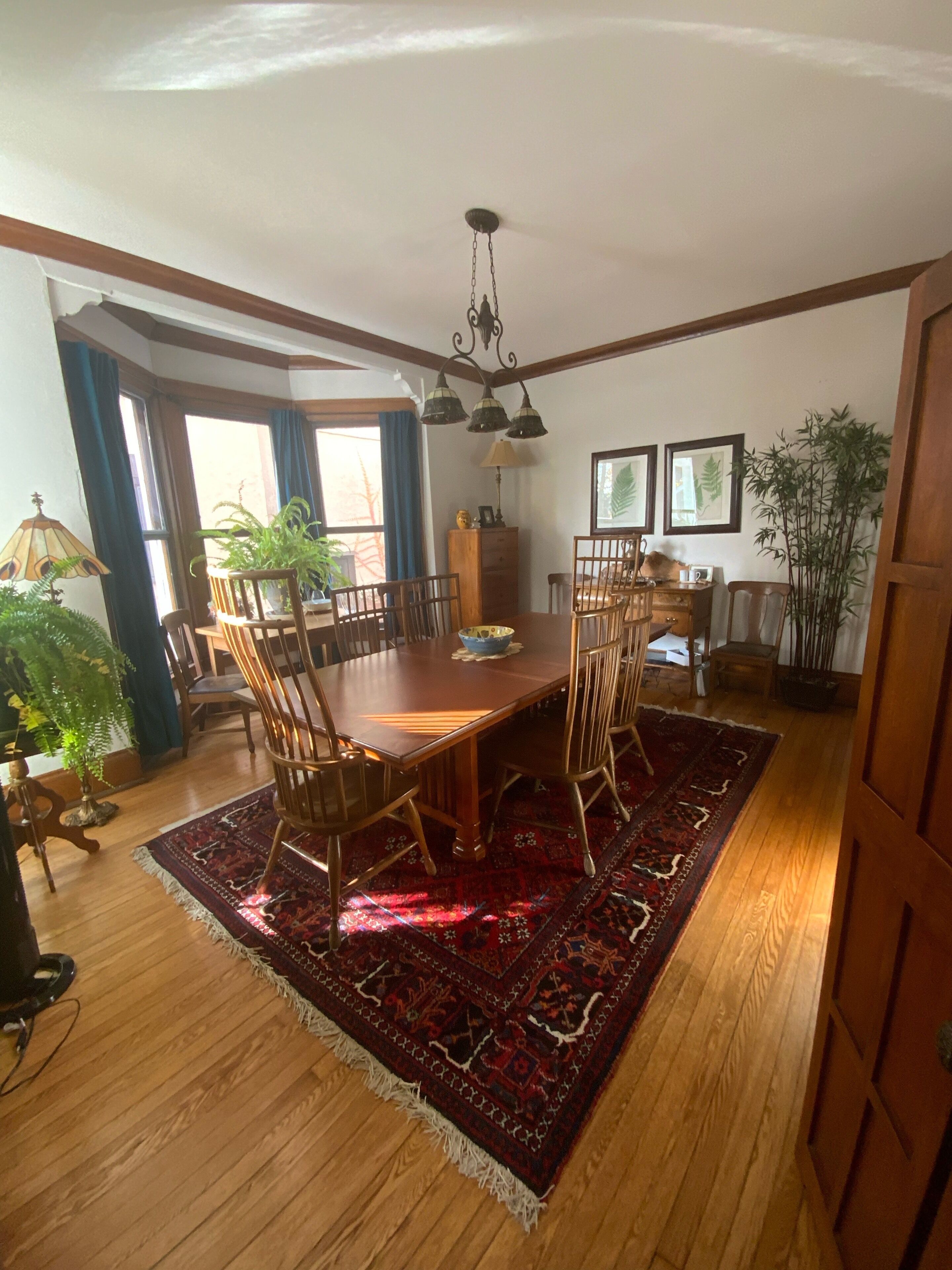 A dining area with a wooden table and chairs, a red patterned rug, and a chandelier.