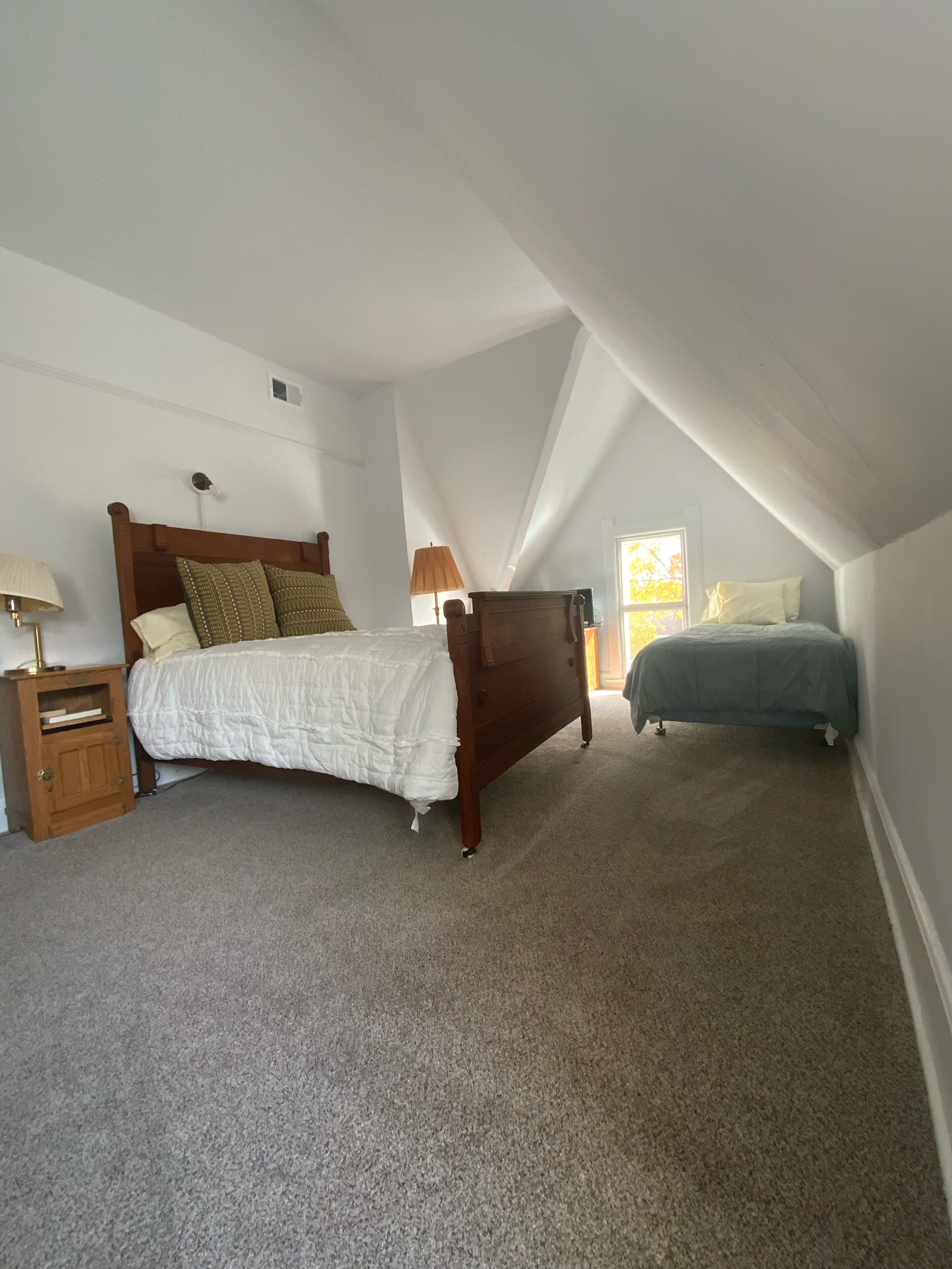 A bedroom with a wooden bed, a nightstand, a dresser, and a window providing natural light.