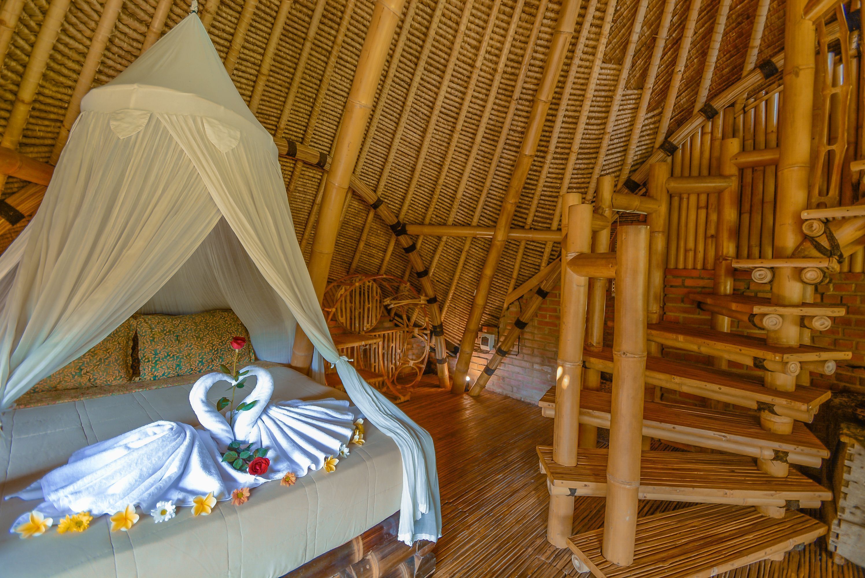 A room with a bed under a canopy, bamboo walls, and a staircase.