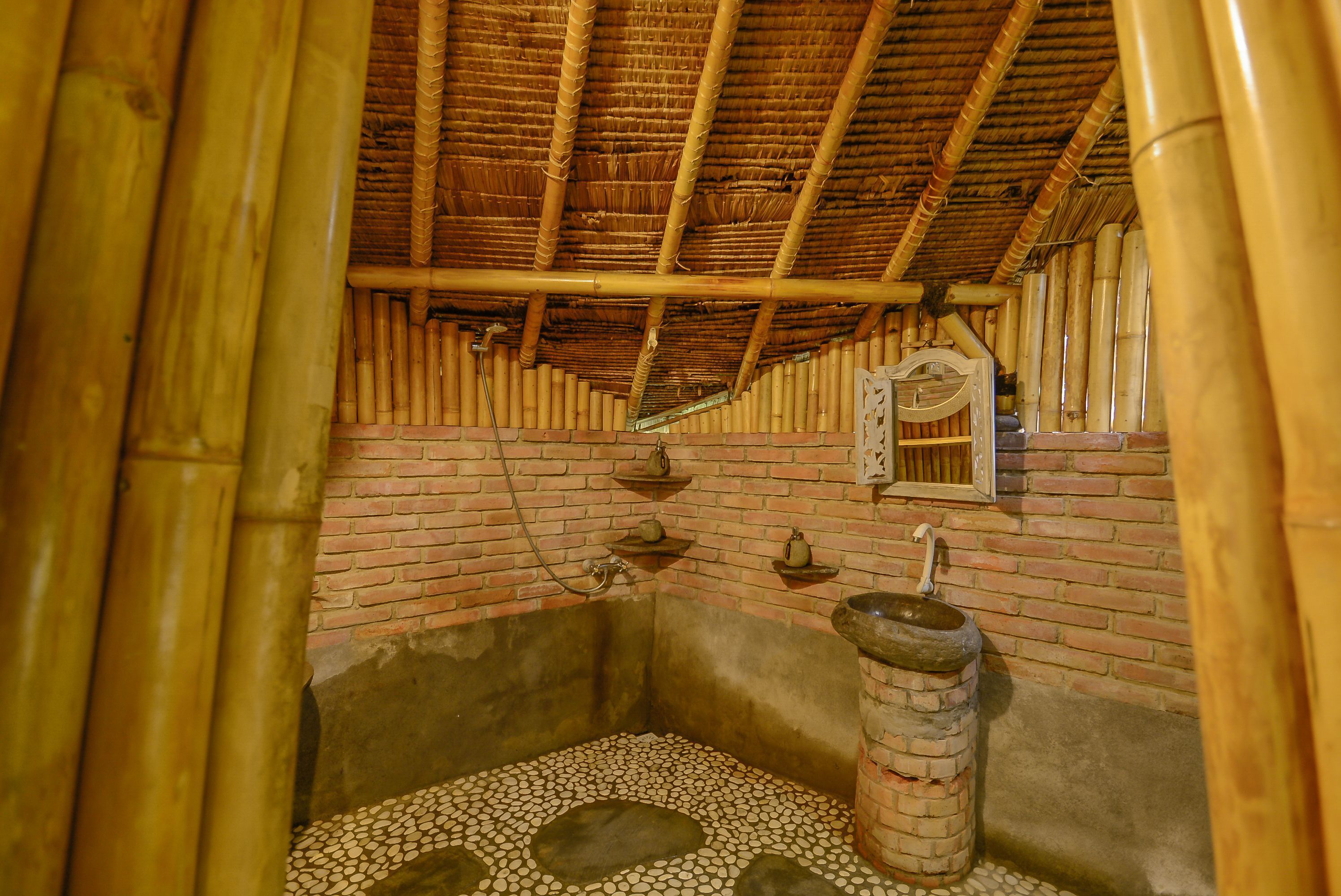 A traditional bamboo-framed room with a brick wall, a stone basin, and a small shelf with a teapot.