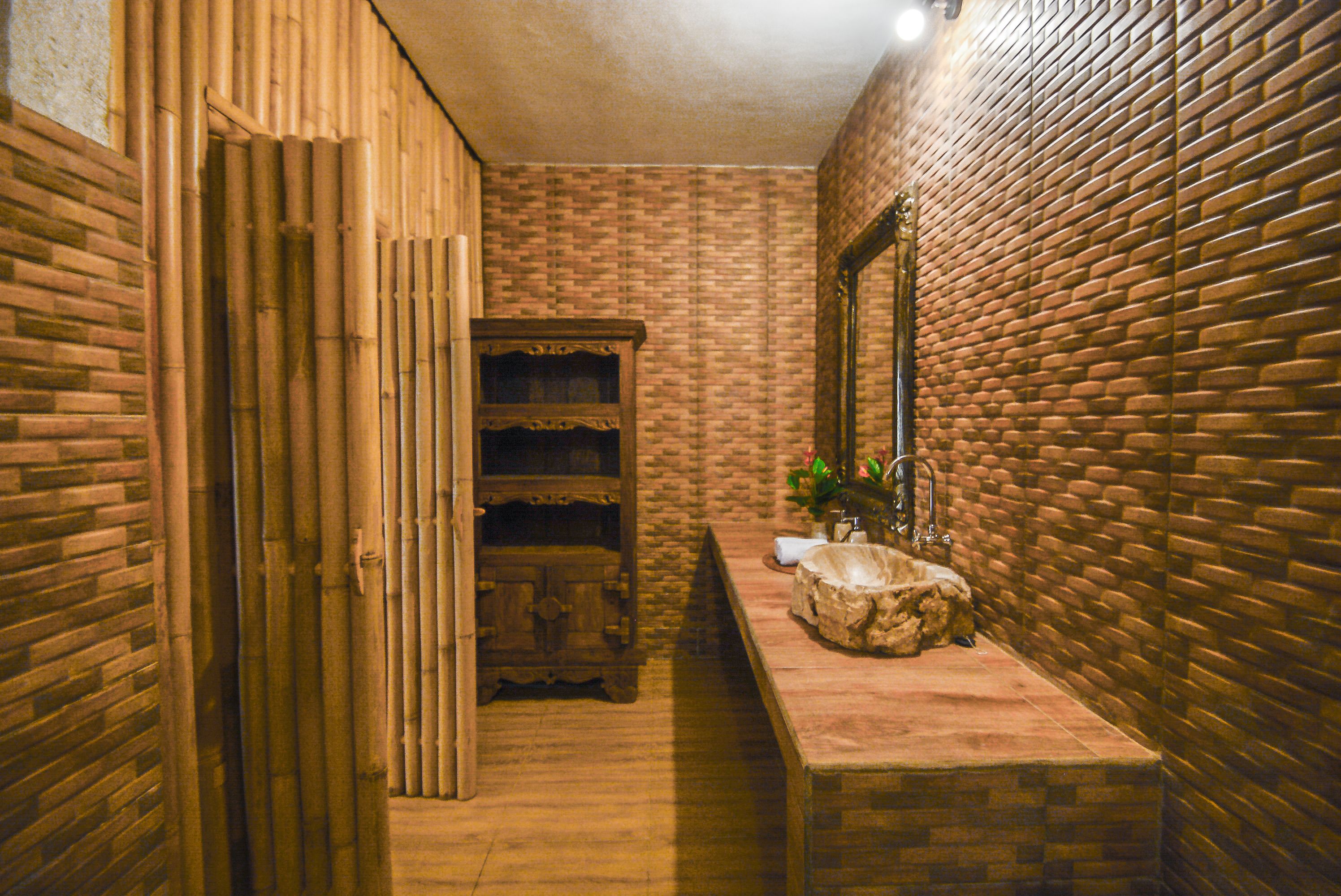 A bathroom with a wooden door, a wooden bench, a sink with a stone basin, and a mirror on the wall.