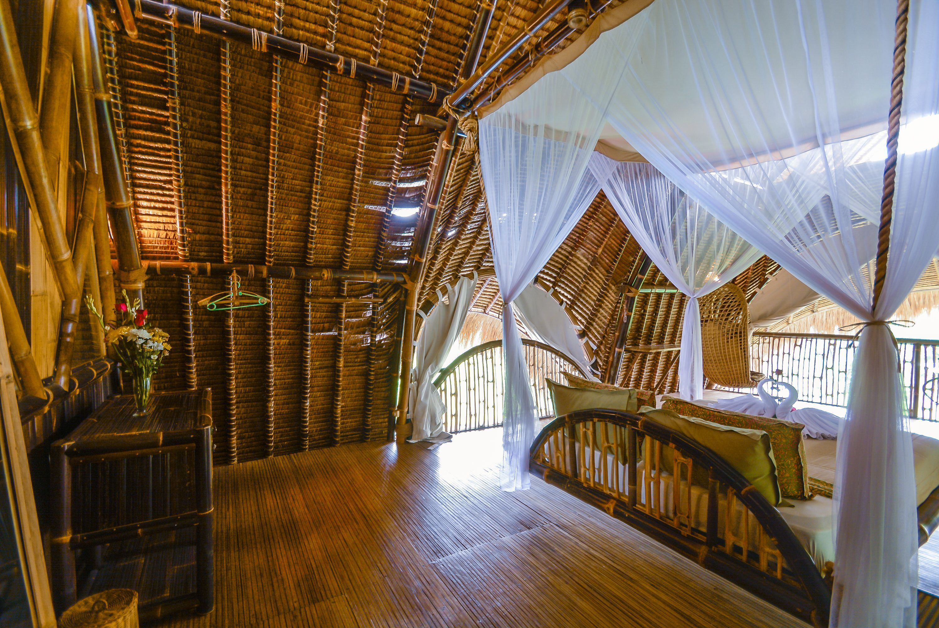 A room with a wooden floor, a bed with a canopy, and a wicker chair.