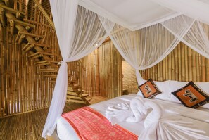 Habitación con cama, dosel blanco, pared de bambú y almohadones decorativos.
