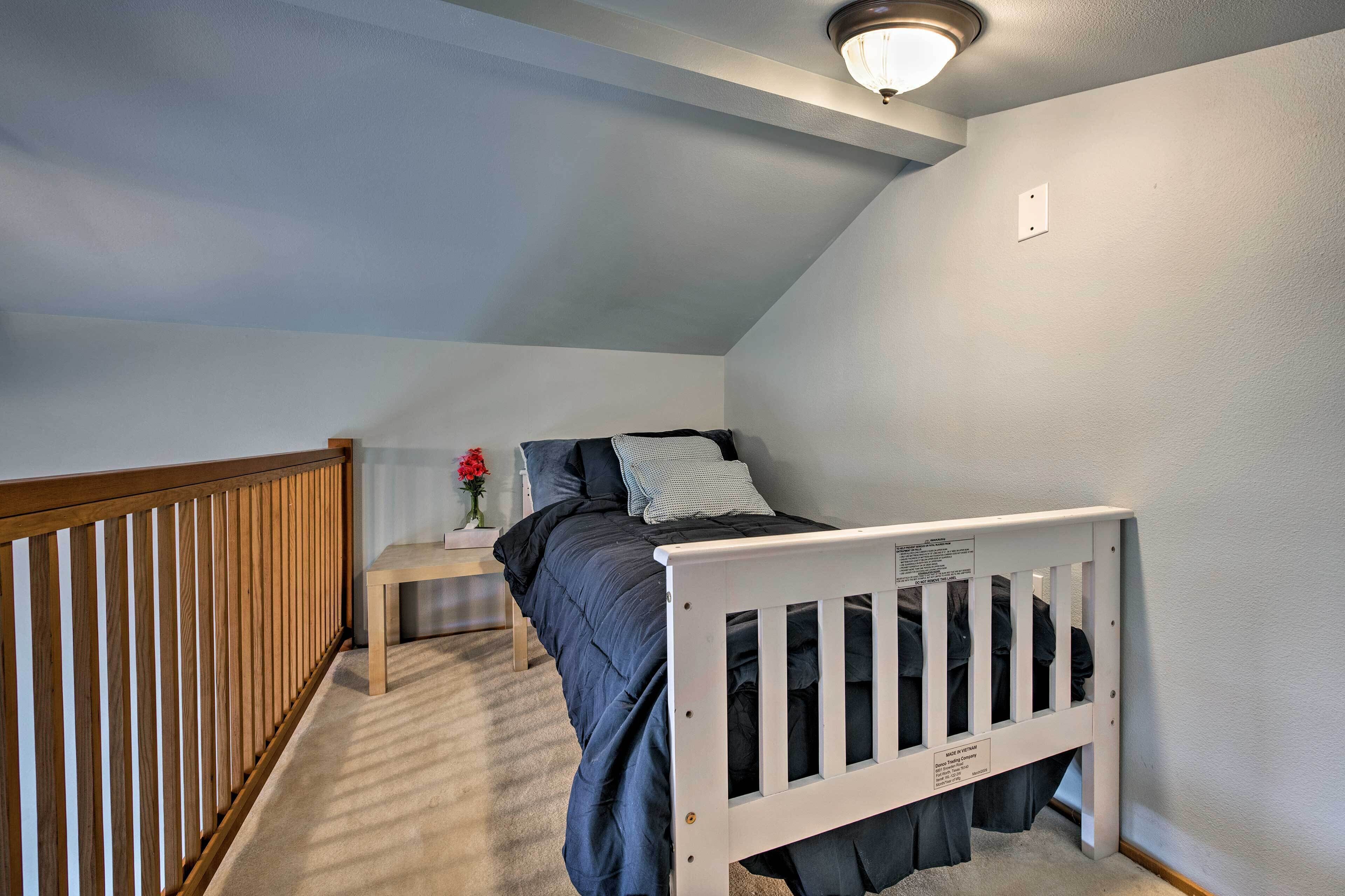 A bedroom with a sloped ceiling, a wooden crib, a bedside table with a vase of flowers, and a white wall.