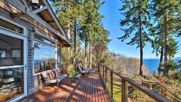 Une terrasse en bois avec un canapé et une table, offrant une vue sur une forêt et l’océan.