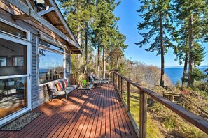 Eine Holzterrasse mit Sofa und Tisch, mit Blick auf einen Wald und den Ozean.
