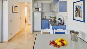 Una cocina moderna con armarios blancos y azules, un microondas y un lavabo. Hay una mesa con frutas y una olla de metal.