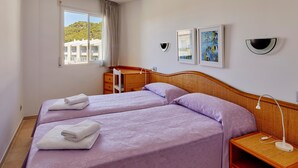 Habitación de hotel con dos camas, un escritorio, una silla, una mesita de noche y una ventana con vistas a edificios.