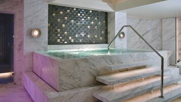 Un moderno espacio de spa con una piscina de mármol, escalones que bajan a la piscina y una pared decorativa.