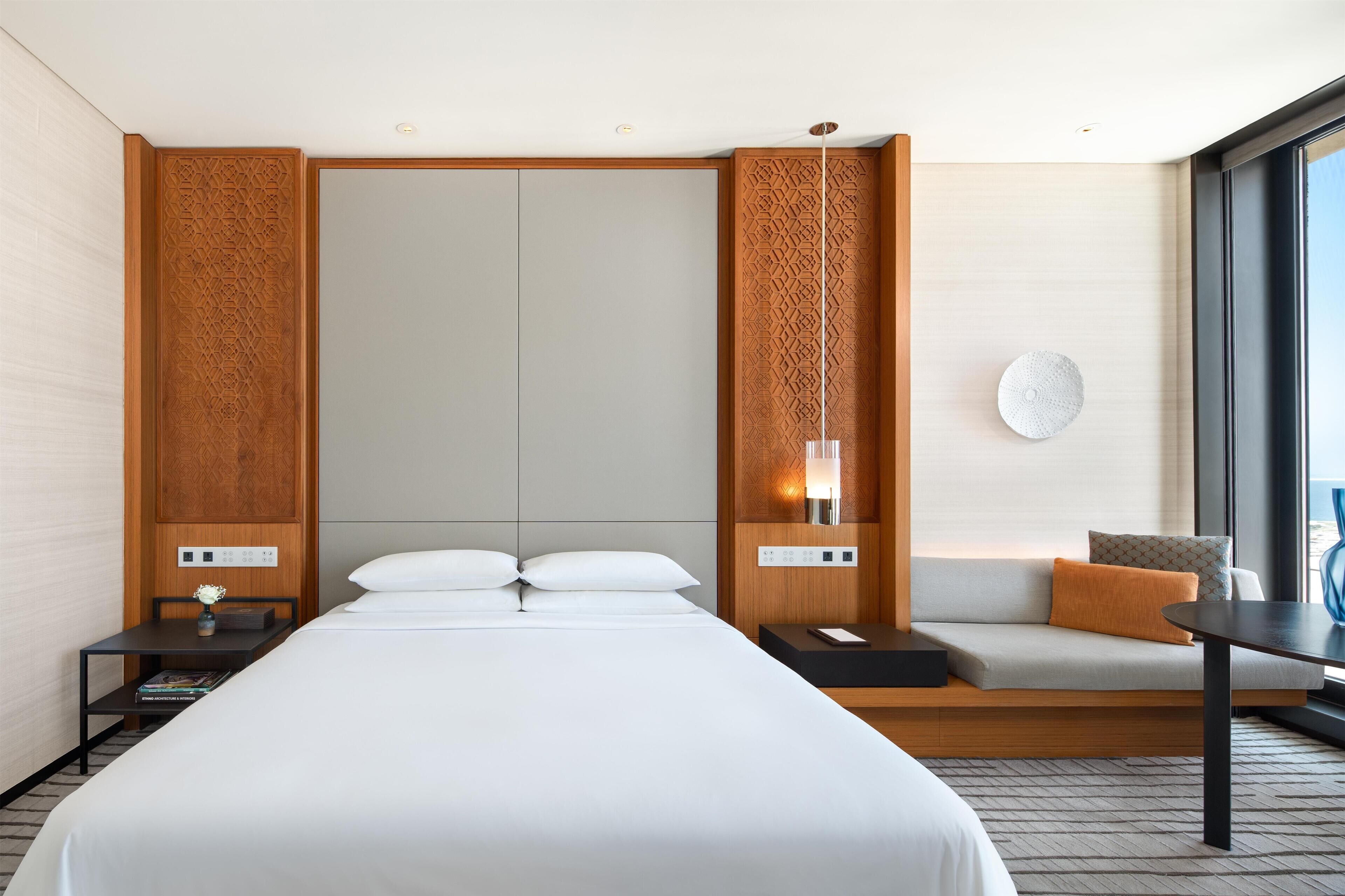 Una habitación de hotel moderna con una cama grande, un sofá, una mesita y una mesita de noche.