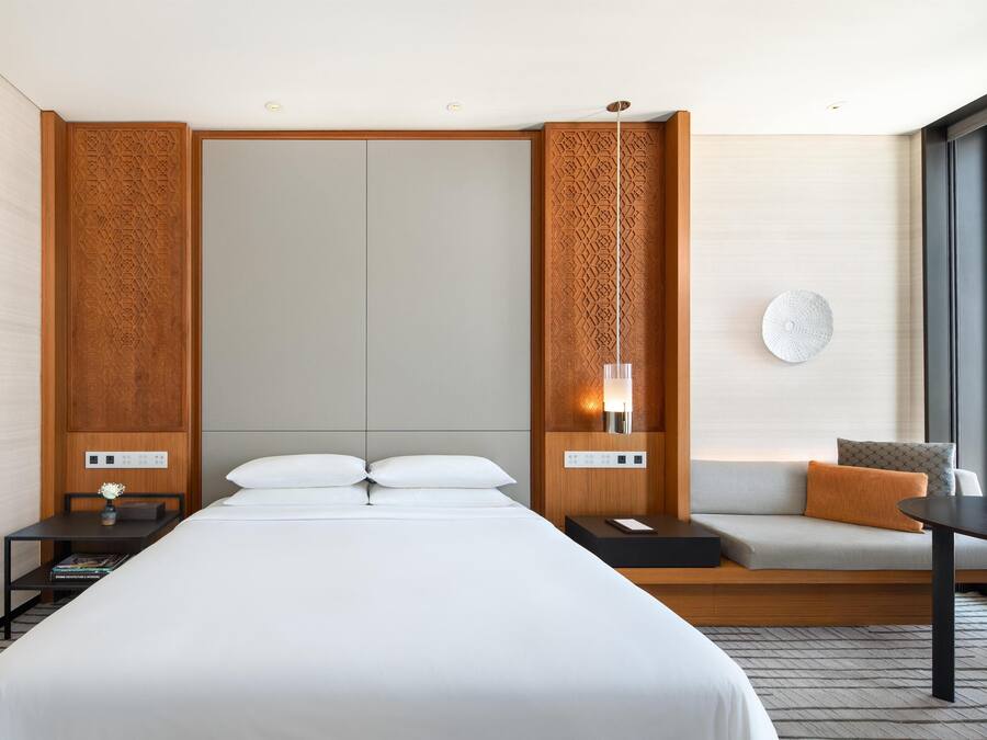 Una habitación de hotel moderna con una cama grande, un sofá, una mesita y una mesita de noche.