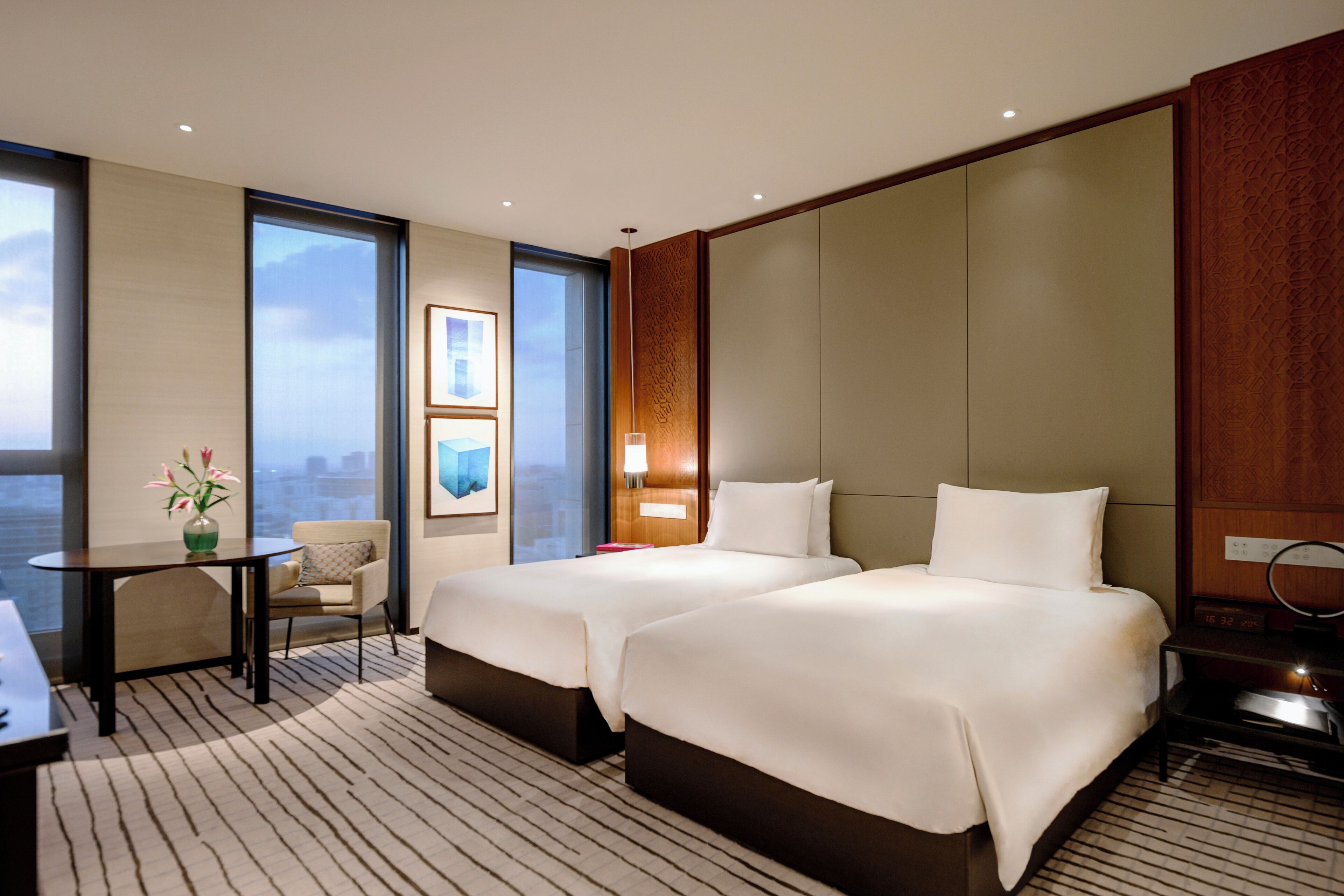 Une chambre d’hôtel avec deux lits, un bureau, une chaise et une grande fenêtre donnant sur la ville.