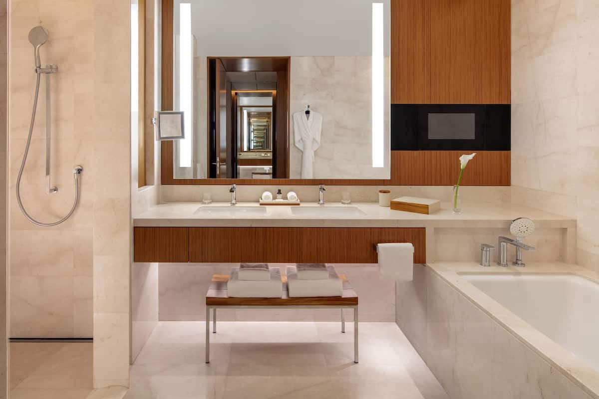 Ein modernes Badezimmer mit großem Spiegel, Holzschränken, einer Sitzbank, einer Badewanne und einer Dusche.