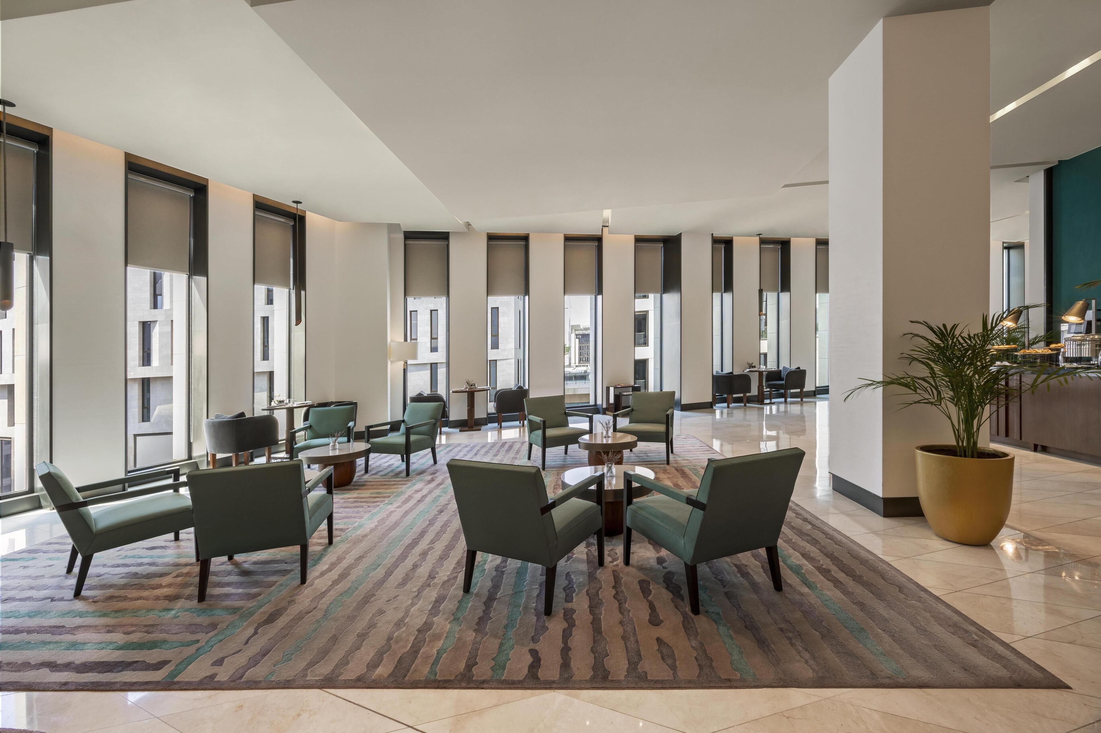 A spacious lobby with multiple seating areas, large windows, and a central plant.