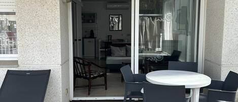 An outdoor patio with a round table and chairs, a wooden deck, and a sliding glass door leading to an interior space with a bed and a dining area.