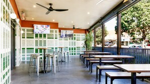 An outdoor dining area with tables and stools, a ceiling fan, and a menu board. - Kingsgrove Hotel (Kingsgrove)