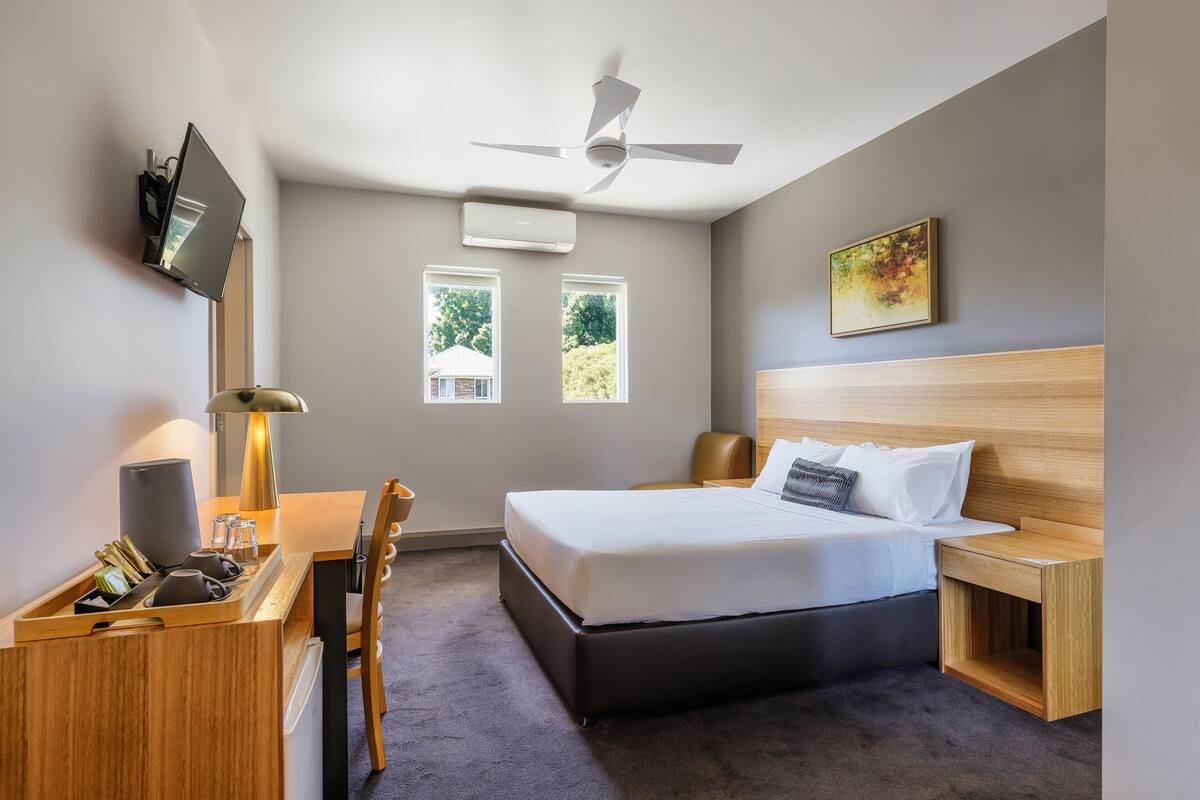 Une chambre d’hôtel moderne équipée d’un lit, d’une table de chevet, d’un bureau, d’une chaise et d’un ventilateur de plafond.