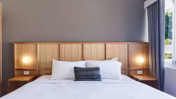 Una cama bien hecha con cabecera de madera, dos mesitas de noche y una mesita con lámpara.