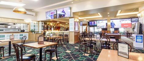 A hotel lobby with multiple seating areas, a bar, and a kitchen visible in the background.