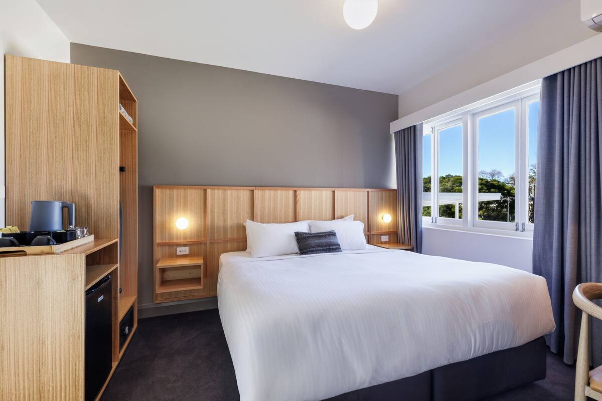 Une chambre d’hôtel avec un grand lit, une armoire en bois, une table de chevet et une vue sur l’extérieur par la fenêtre.