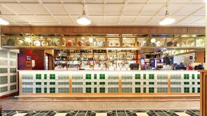 A bar area with a tiled counter, shelves with bottles, and a patterned carpet. - Kingsgrove Hotel (Kingsgrove)