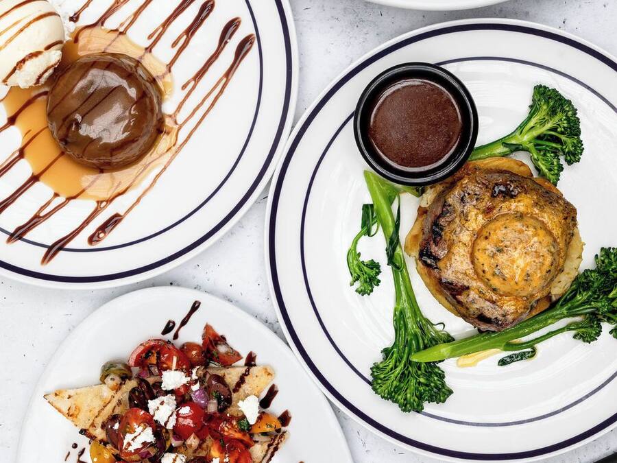 Diversos pratos em chapas, incluindo uma sobremesa com calda de caramelo, um prato de carne acompanhado de brócolis e uma salada com queijo feta.