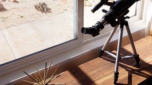 Un télescope monté sur un trépied, placé près d’une grande fenêtre donnant sur un paysage désertique.
