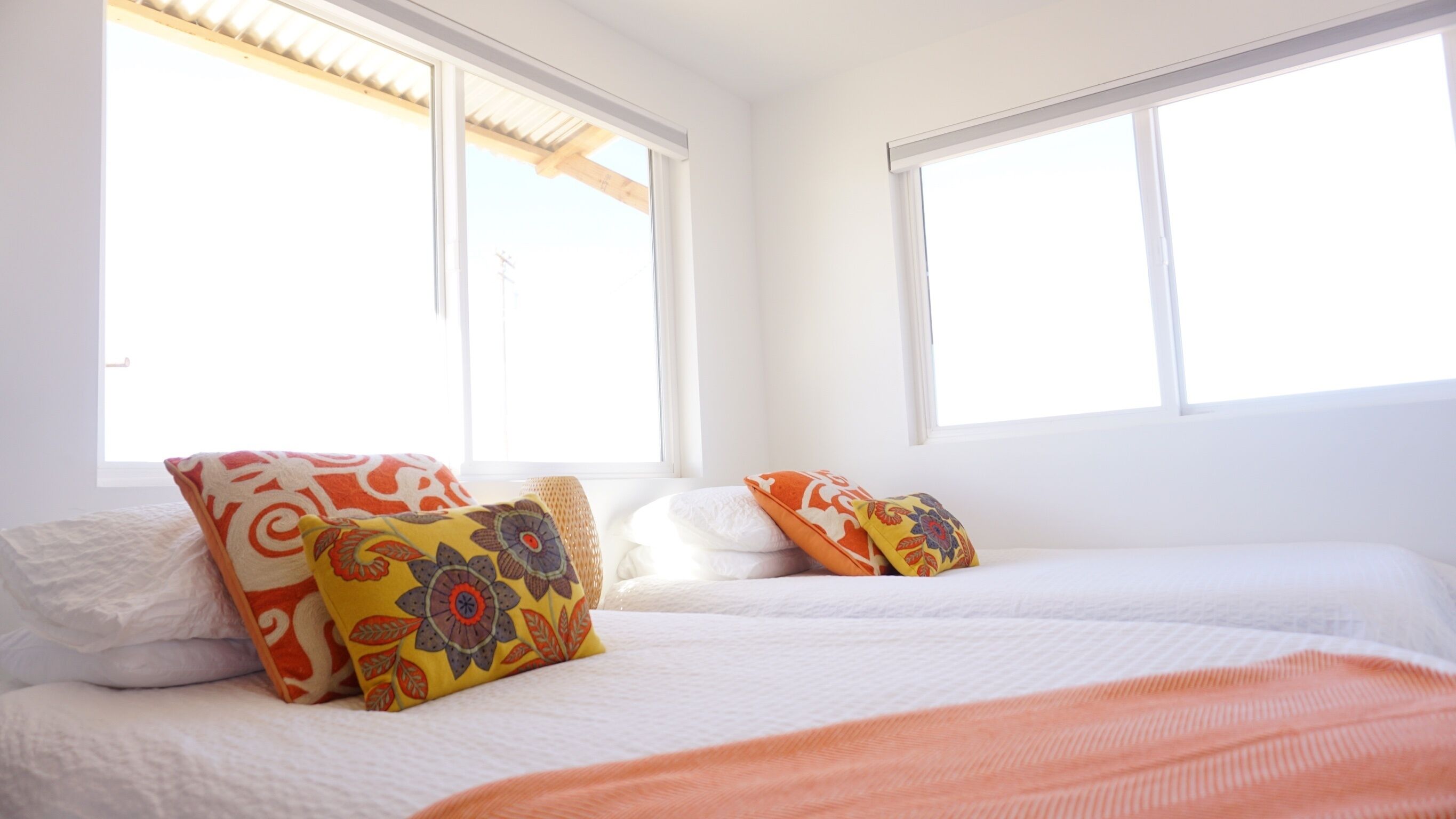 Ein Schlafzimmer mit zwei Betten, weißer Bettwäsche und bunten Kissen.