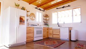 Une cuisine avec des meubles en bois, un réfrigérateur blanc, une cuisinière, un évier et un lave-vaisselle. On y trouve des fenêtres avec des poutres en bois, un tapis et un élément décoratif mural.