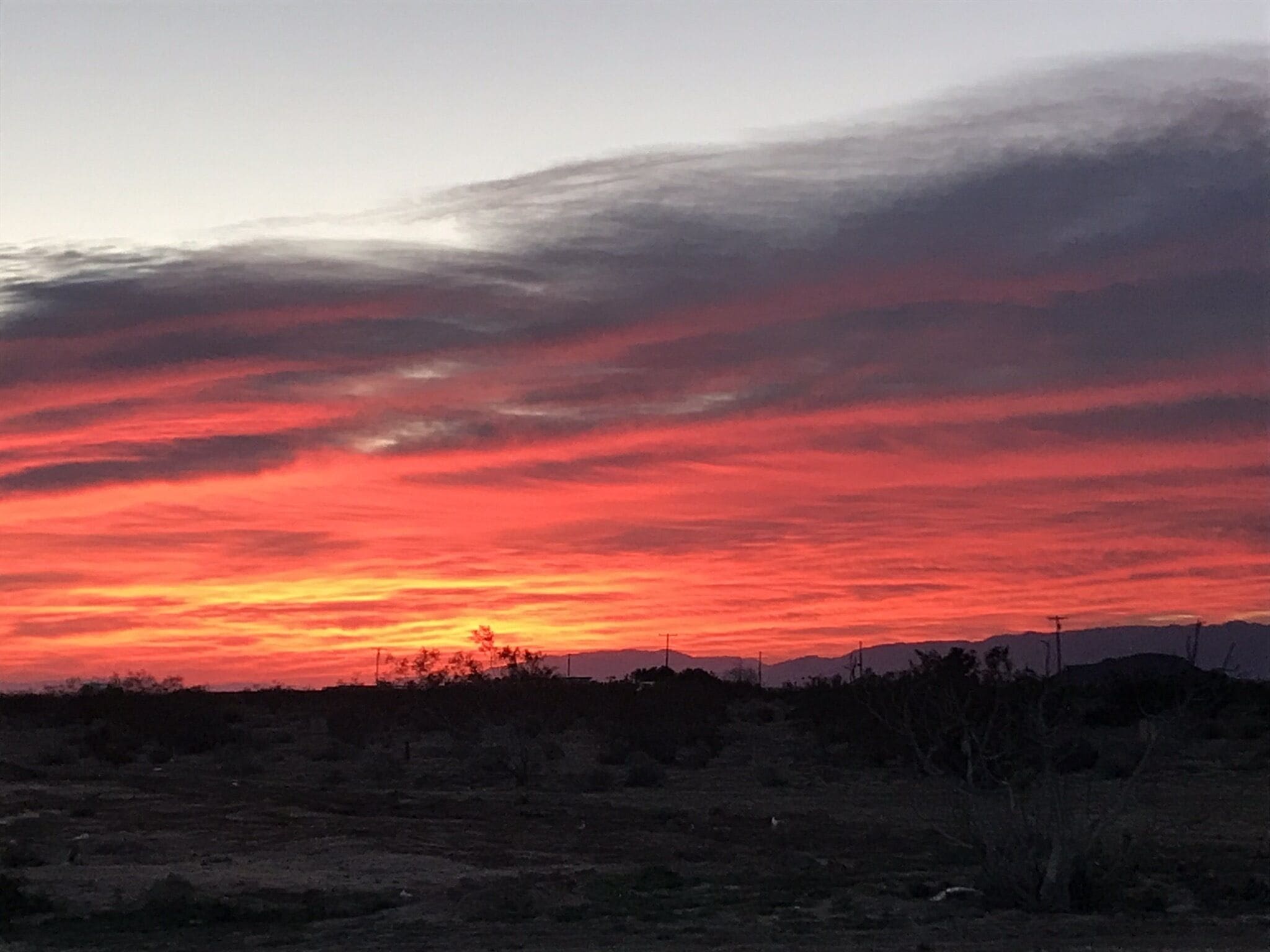 A sunset over a flat landscape with sparse vegetation and distant hills.