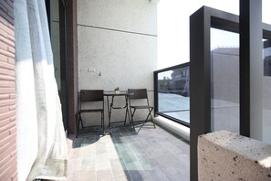 Uma varanda com mesa e duas cadeiras, vista para a rua e um edifício ao fundo.